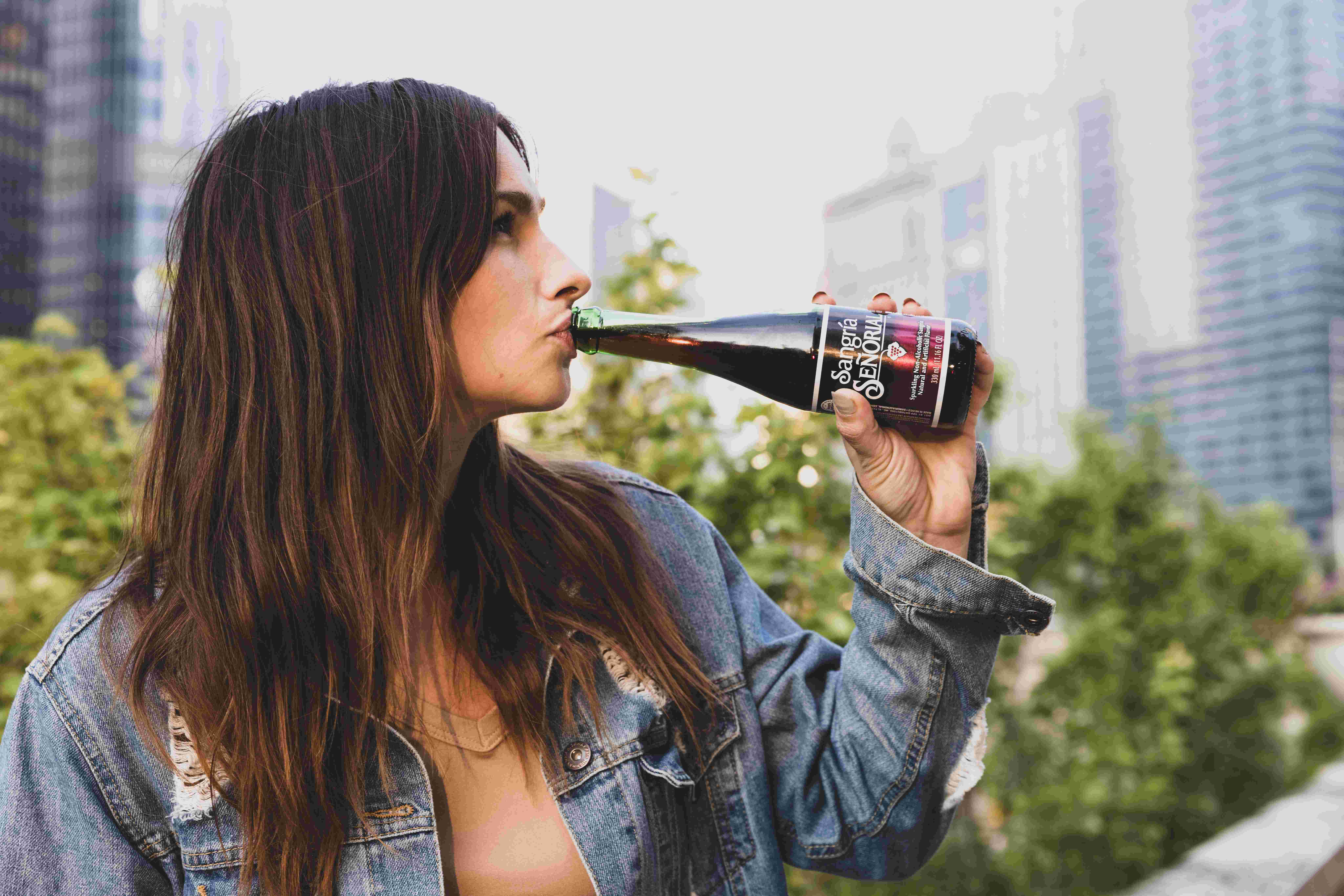 Žena drží v ústech lahev s alkoholem a popíjí.